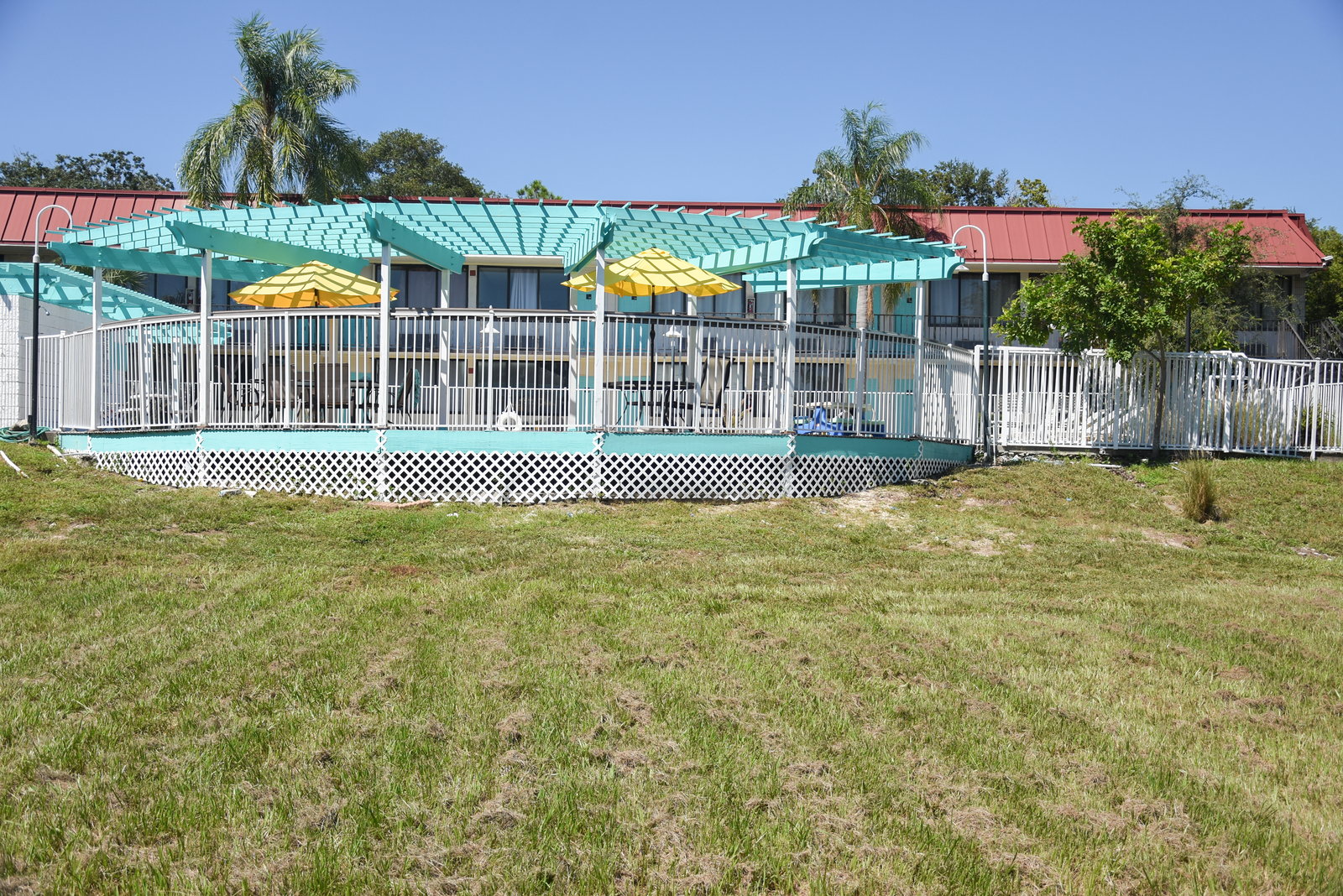 Terraza de la piscina con pérgola y sombrillas, vista desde el jardín